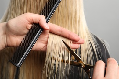 Photo of Hairdresser cutting client's hair with scissors on light grey background, closeup