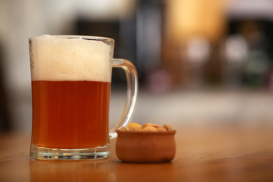 Photo of Pint of cold tasty beer served with peanuts on wooden table