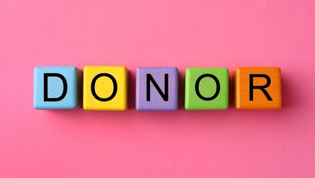 Photo of Word Donor made of colorful wooden cubes on pink background, flat lay