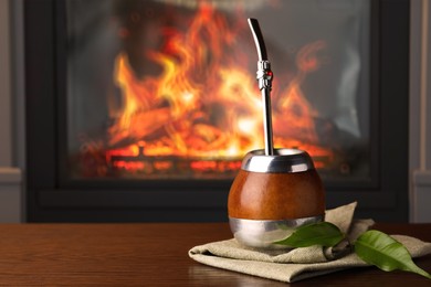 Image of Calabash with mate tea and bombilla on wooden table near fireplace. Space for text