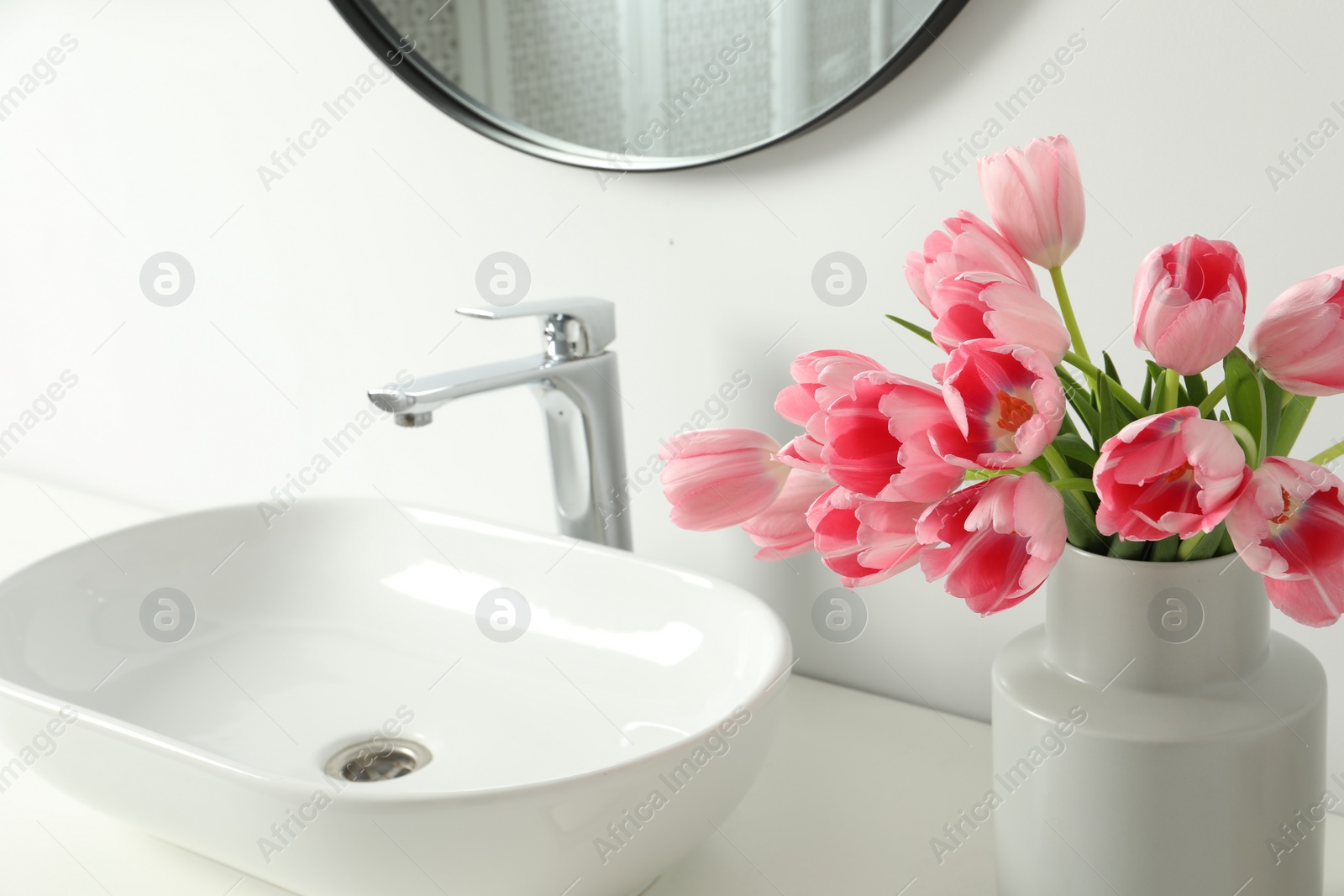 Photo of Vase with beautiful pink tulips near sink in bathroom