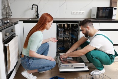Photo of Woman looking how serviceman repairing her dishwasher in kitchen