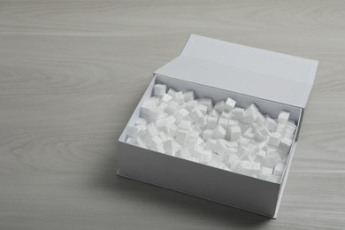Photo of Cardboard box with styrofoam cubes on wooden floor. Space for text