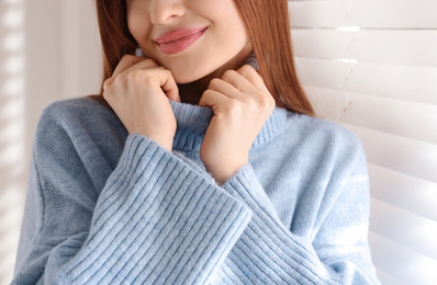 Photo of Young woman wearing warm sweater near window at home, closeup. Winter season