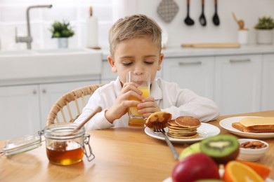 Photo of Breakfast time. Cute little boy drinking juice at table in kitchen