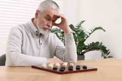 Photo of Playing checkers. Concentrated senior man thinking about next move at table in room
