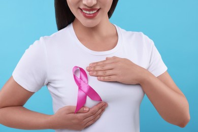 Photo of Woman with pink ribbon on light blue background, closeup. Breast cancer awareness