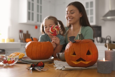 Photo of Mother and daughter making pumpkin jack o'lantern at table in kitchen. Halloween celebration