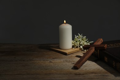 Photo of Church candle, flowers, cross and Bible on wooden table, space for text