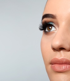 Photo of Young woman with eyelash extensions and beautiful makeup on light background. Space for text