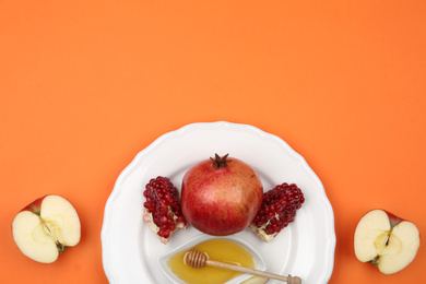Photo of Honey, apples and pomegranate on orange background, flat lay. Rosh Hashanah holiday