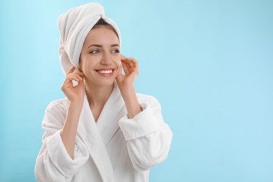 Beautiful young woman with hair wrapped in towel after washing on light blue background. Space for text