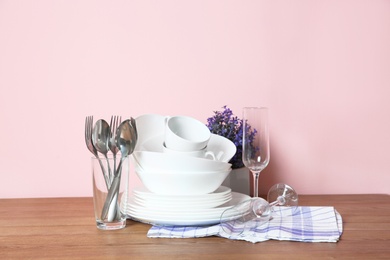 Photo of Set of clean dishes and cutlery on table against color background