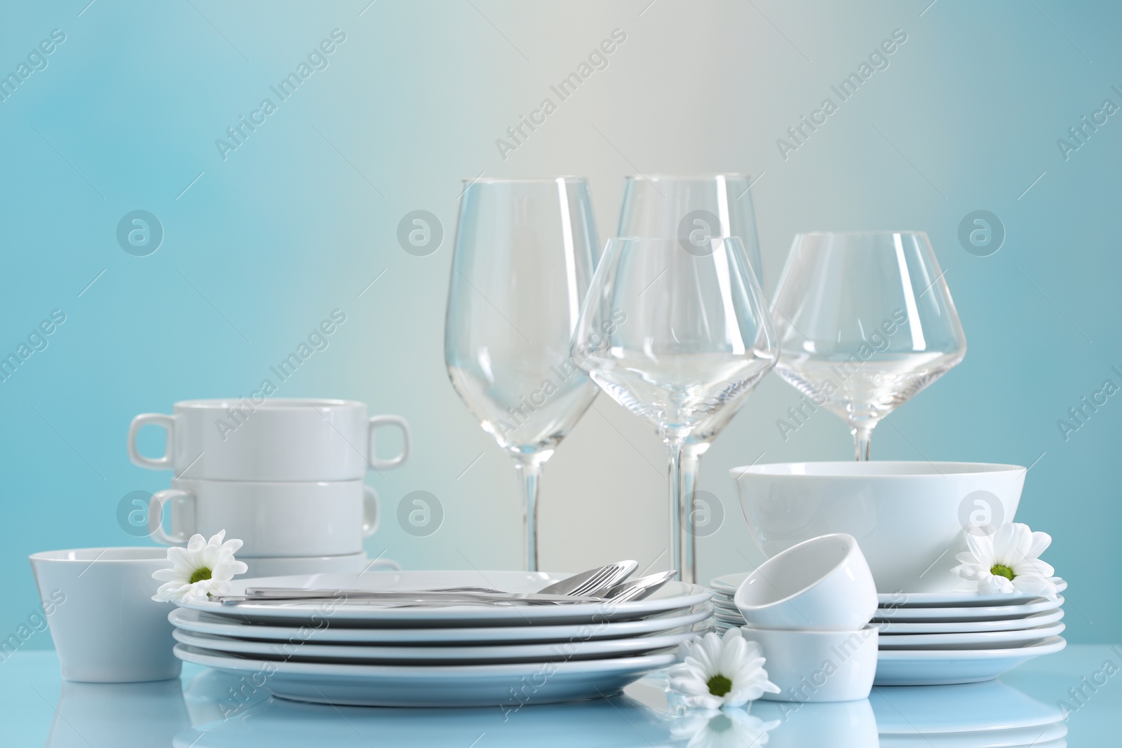 Photo of Set of many clean dishware, cutlery, flowers and glasses on light blue table