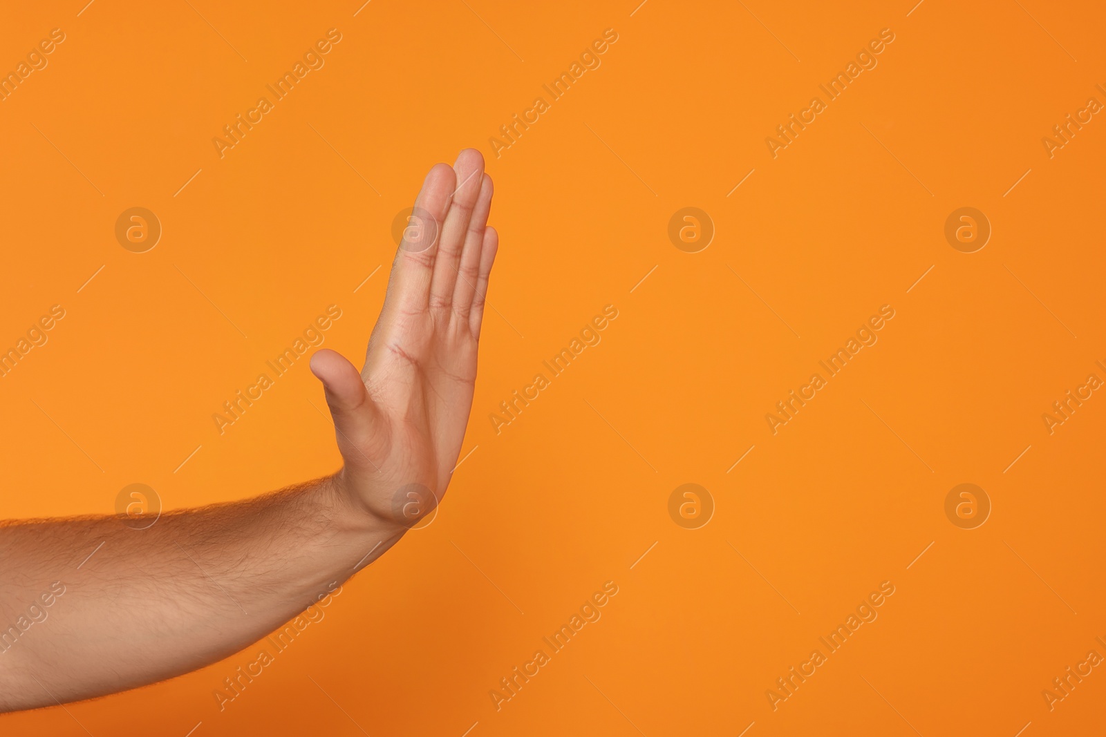 Photo of Man showing stop gesture on orange background, closeup with space for text