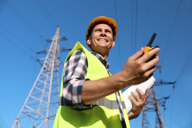 Photo of Professional electrician with portable radio station near high voltage tower