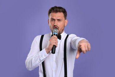 Photo of Handsome man with microphone singing on violet background