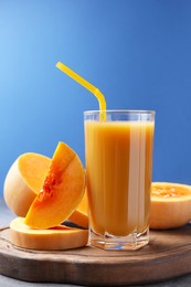 Photo of Tasty pumpkin juice in glass and cut pumpkin on light grey table against blue background