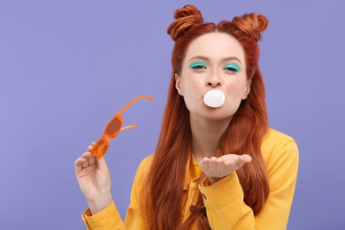 Photo of Portraitbeautiful woman with bright makeup blowing bubble gum on violet background