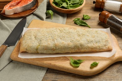 Photo of Delicious strudel with salmon and spinach on wooden table, closeup