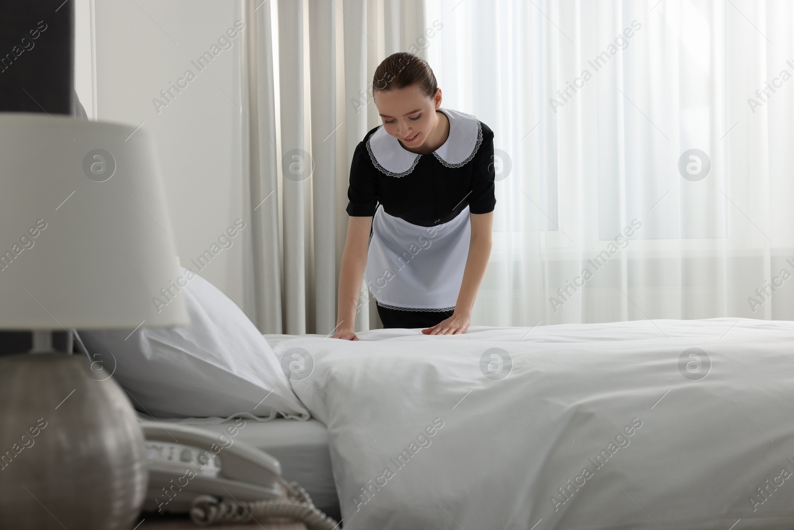 Photo of Young maid making bed in hotel room