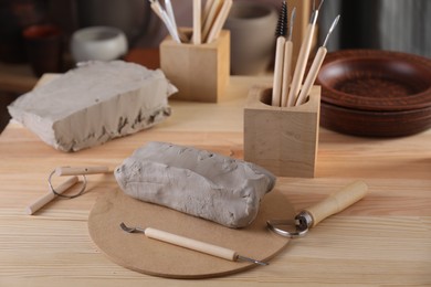 Photo of Clay and set of modeling tools on wooden table in workshop