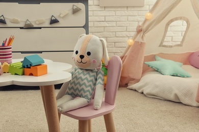 Photo of Cute toy bunny on small chair in playroom. Interior design
