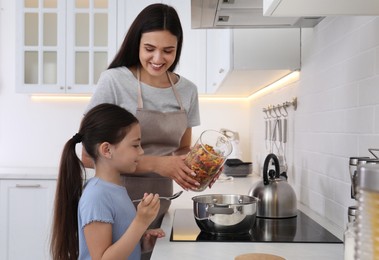 Photo of Little girl helping her mother with cooking in kitchen. Single parenting