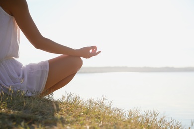 Photo of Young woman meditating near river at sunset, closeup view with space for text. Nature healing power