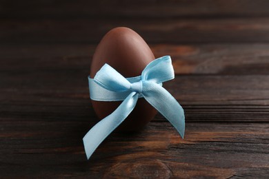 Tasty chocolate egg with light blue bow on wooden table