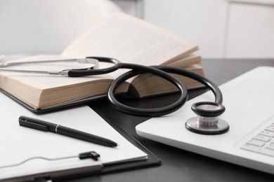 Photo of Open student textbook, clipboard and stethoscope near laptop on grey table indoors, closeup. Medical education