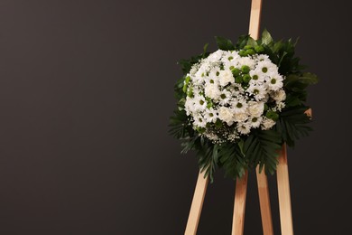 Funeral wreath of flowers on wooden stand against grey background, space for text