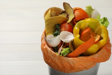 Photo of Trash bin with organic waste for composting on white wooden background, closeup