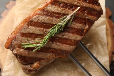 Photo of Delicious grilled beef steak and rosemary on parchment paper, top view
