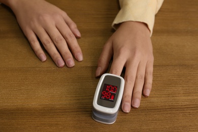 Photo of Woman using pulse oximeter for oxygen level testing at wooden table, closeup