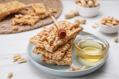 Photo of Delicious peanut bars (kozinaki) and dipper with honey on white marble table, closeup
