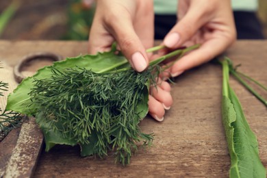 Photo of Woman with fresh green herbs at wooden table, closeup