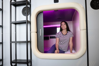 Photo of Happy young woman sitting in capsule of pod hostel