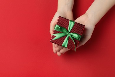 Photo of Woman holding beautifully wrapped Christmas gift box on red background, top view. Space for text
