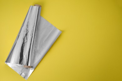 Photo of Roll of aluminum foil on yellow background, top view. Space for text