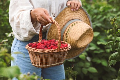 Photo of Woman holding wicker basket with ripe raspberries outdoors, closeup