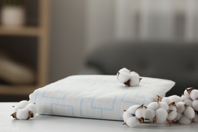 Bed sheet and cotton branch with fluffy flowers on white wooden table in room, closeup