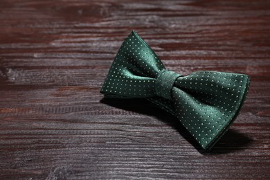 Photo of Stylish green bow tie with polka dot pattern on wooden table, closeup. Space for text