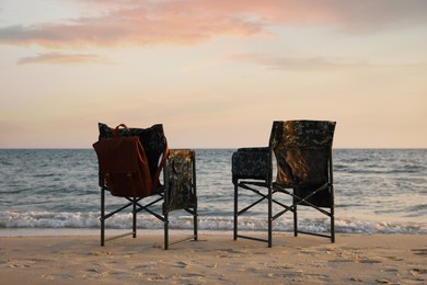 Photo of Camping chairs and backpack on sandy beach near sea