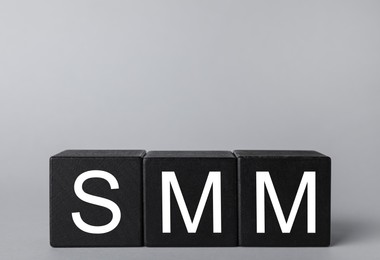 Photo of Black cubes with abbreviation SMM (Social media marketing) on grey background