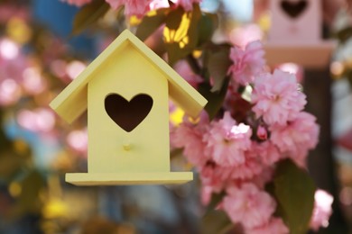 Yellow bird house with heart shaped hole hanging on tree branch outdoors. Space for text