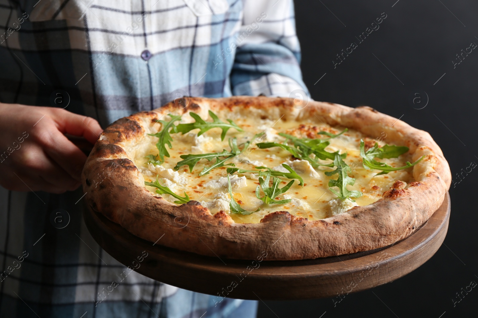 Photo of Woman holding delicious cheese pizza with arugula on black background, closeup