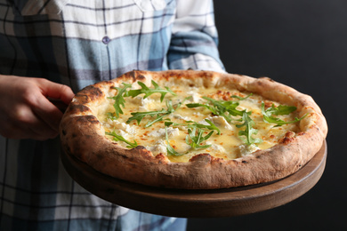 Woman holding delicious cheese pizza with arugula on black background, closeup