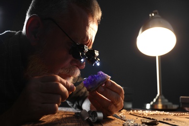 Photo of Male jeweler evaluating amethyst at table in workshop