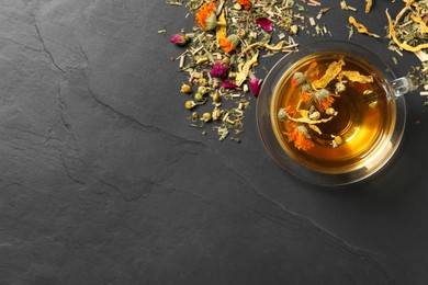 Photo of Freshly brewed tea and dried herbs on black table, flat lay. Space for text